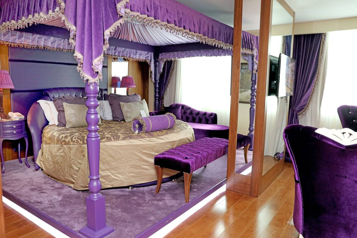 A bedroom with a four-poster bed, a bench, a vanity, and a mirror.