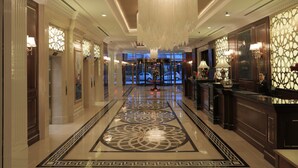 A hotel lobby with a central chandelier, a reception desk, and a patterned floor.