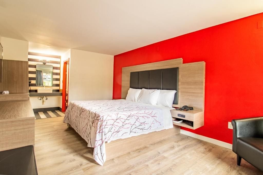 A modern bedroom with a bed, a bedside table, and a red accent wall.