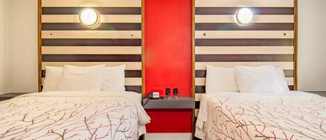 Quarto de hotel com duas camas, uma parede de destaque vermelha e uma pequena mesa com telefone e luminária.