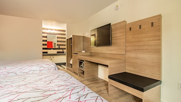 Ein modernes Hotelzimmer mit einem großen Bett, einem an der Wand montierten Fernseher und integrierten Stauraumeinheiten.