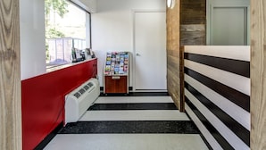 Ein Flur mit roter Wand, weißer Wand, Holzwand, Boden in Schwarzweiß-Streifen, einer Tür, einem Fenster und einem Magazinbord.