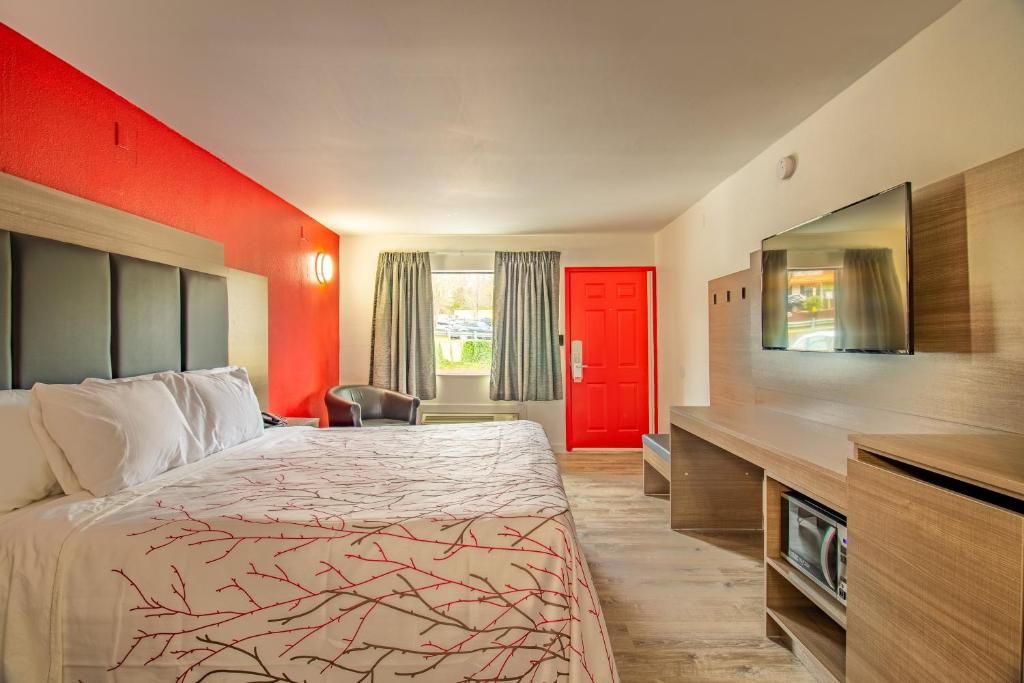 A hotel room with a bed, a desk, a TV, and a red door.