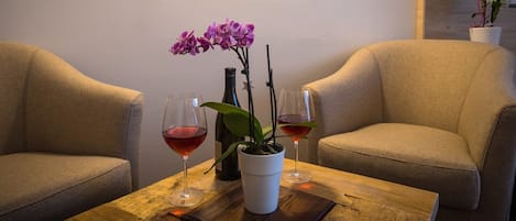 Twee fauteuils, een houten tafel met twee wijnglazen en een fles, en een potorkidee.