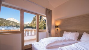 A hotel room with a large bed, a nightstand, a lamp, and a view of mountains through a large window.