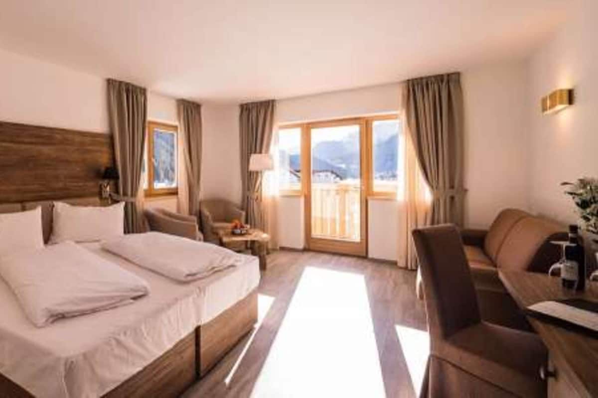 A hotel room with a large bed, a desk, a chair, and a view of mountains through the windows.