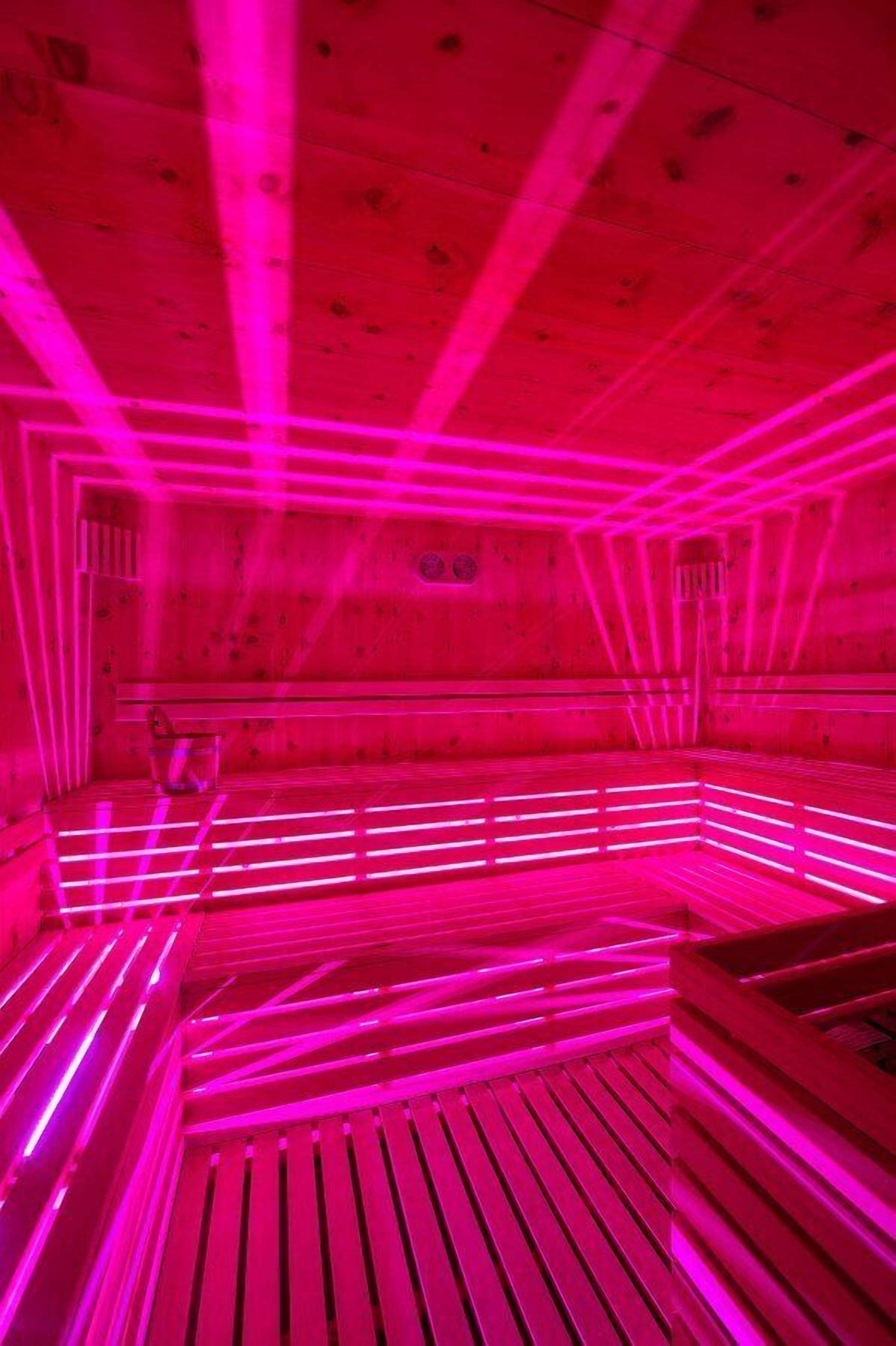 A sauna with wooden benches and pink lighting.