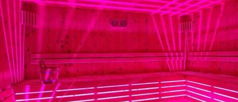 A sauna with wooden benches and pink lighting.