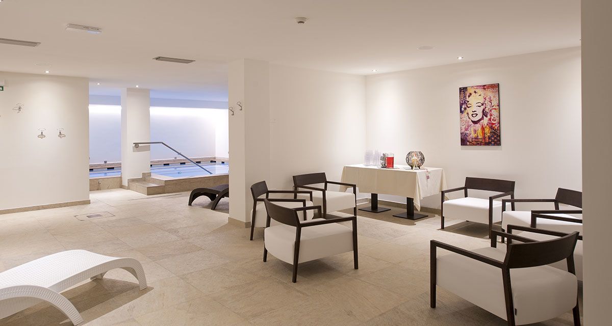 A modern hotel lobby with a pool view, seating area, and artwork on the wall.