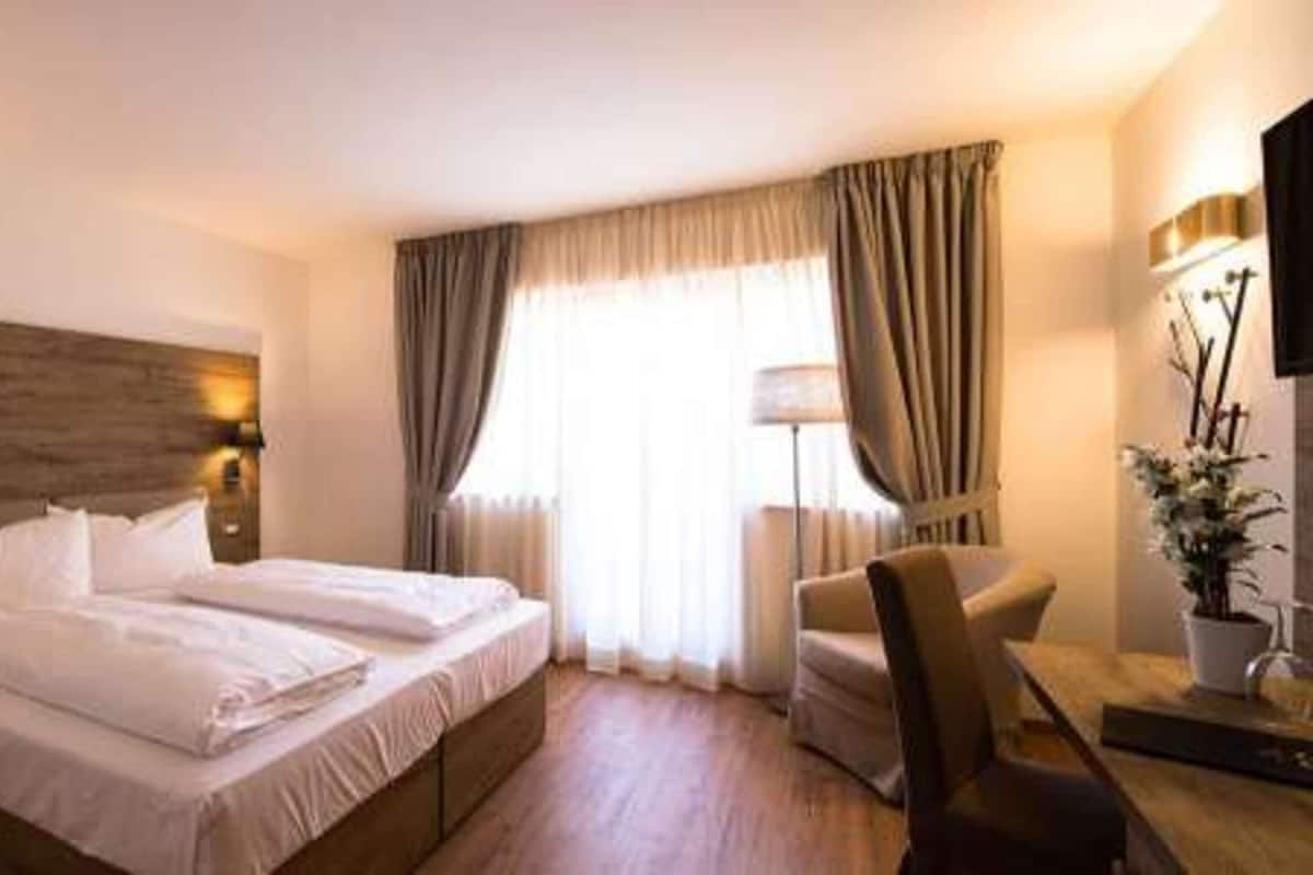 A hotel room with a large bed, bedside tables, a chair, a desk, and a lamp.