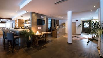 Un hall d’hôtel moderne doté d’un bar, de coins salon et d’une grande plante.