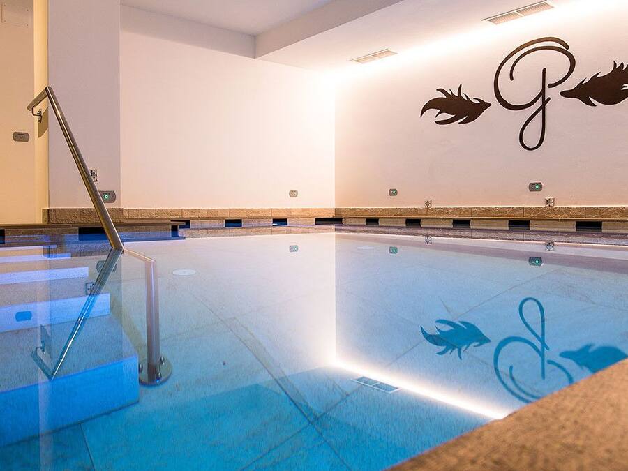 A swimming pool with a glass barrier, a shower area, and a wall with a logo.