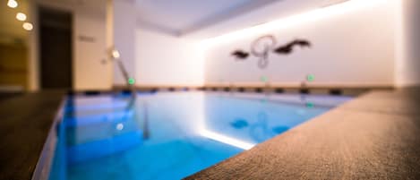 Una piscina con borde de madera, una pared con un logotipo e iluminación empotrada.