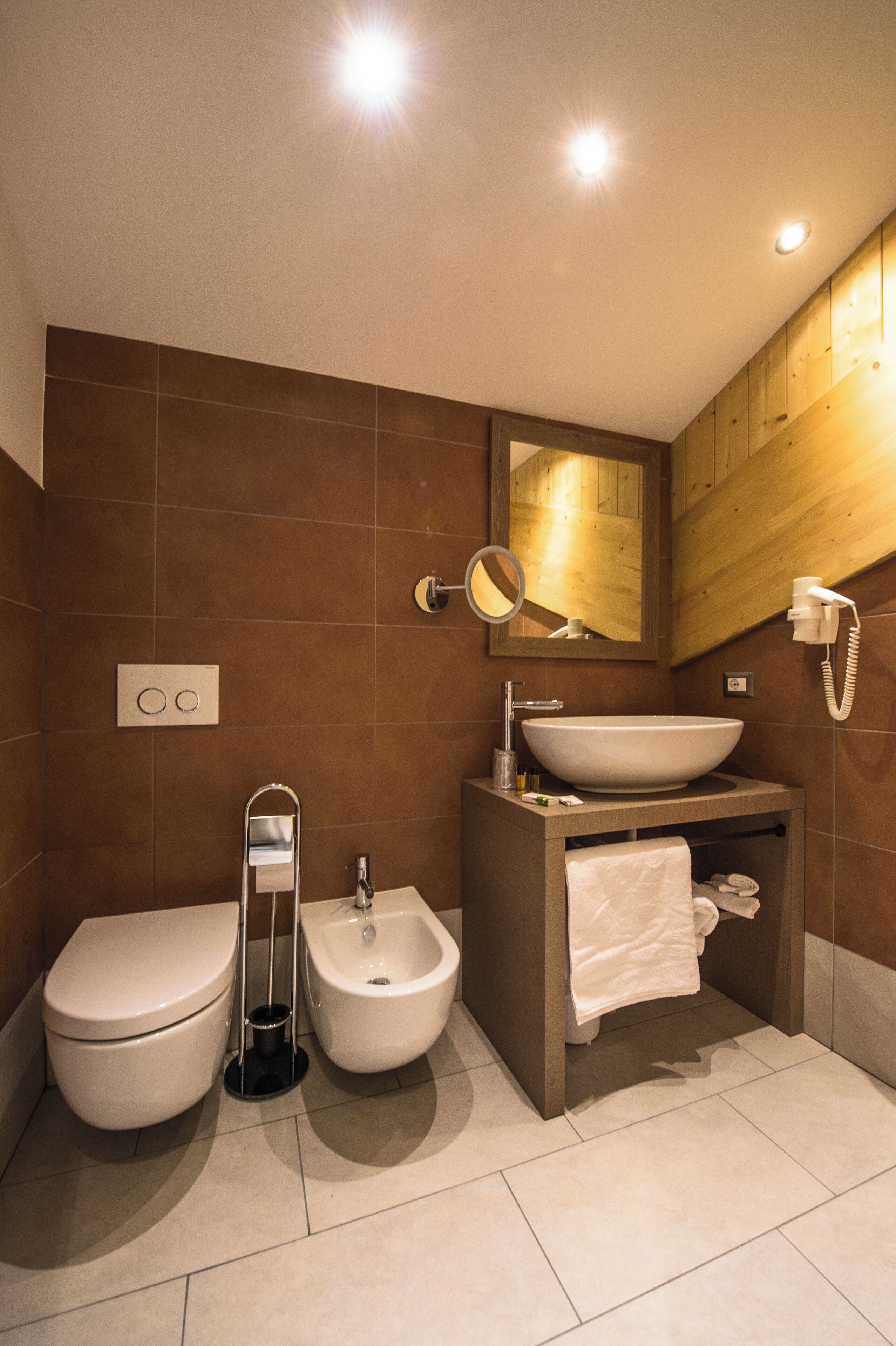 Un baño moderno con inodoro, bidé, tocador con lavamanos, espejo y toallero.