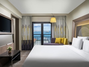Une chambre d’hôtel avec un grand lit, une télévision, un bureau et une vue sur la mer.