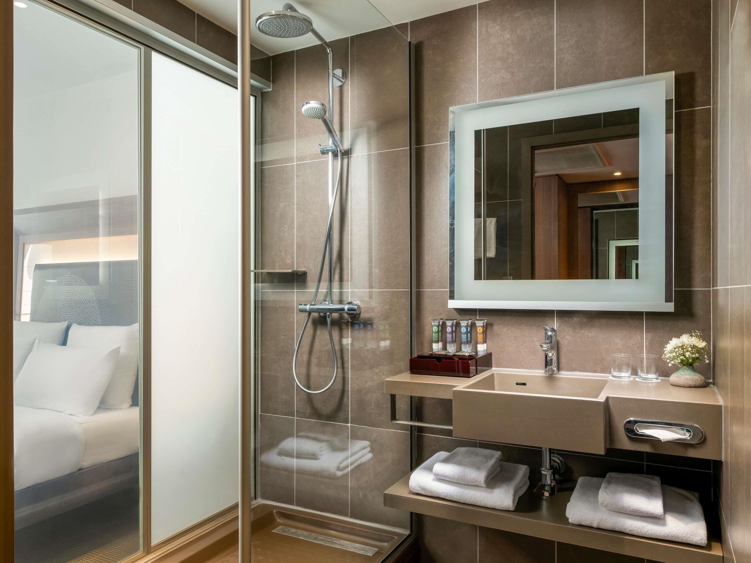 Un bany modern amb un plat de dutxa de vidre, un mirall gran, un lavabo amb calaixera i tovalloles ben arrufades.
