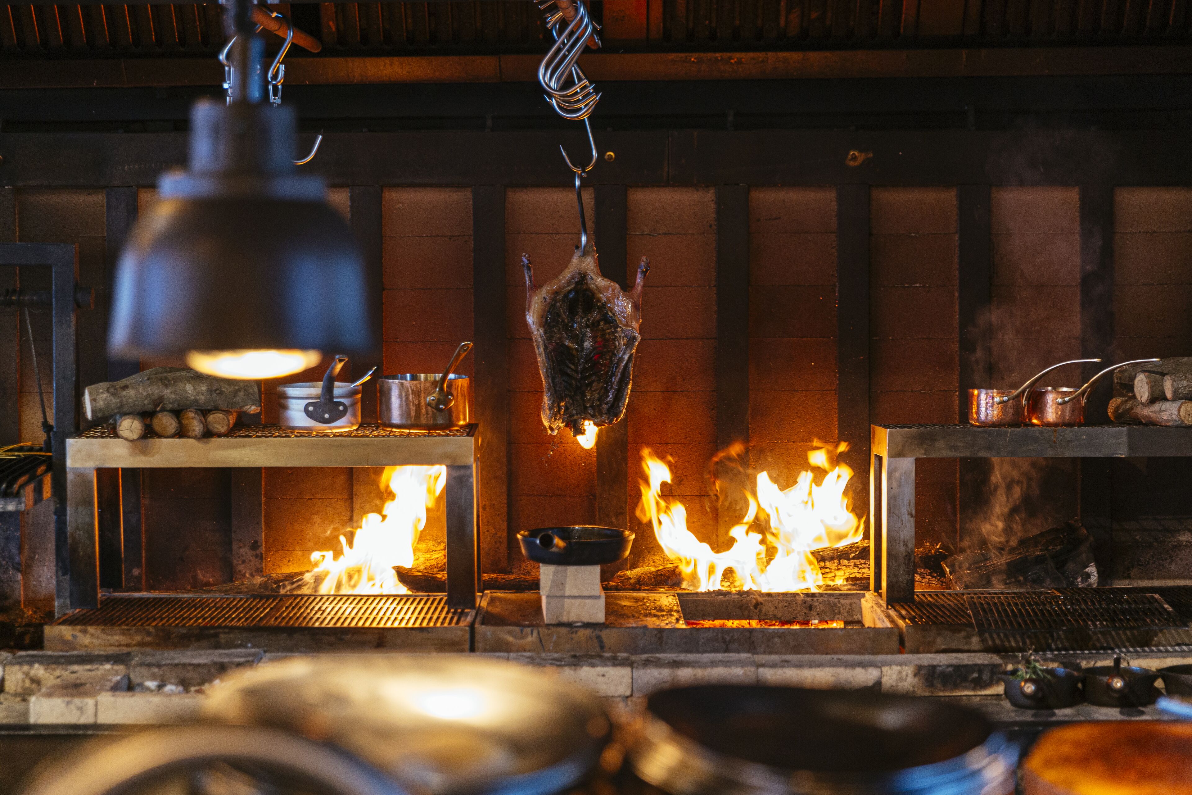 Een traditionele open vuur kookopstelling met opgehangen vlees, een hangende lamp en een grill.