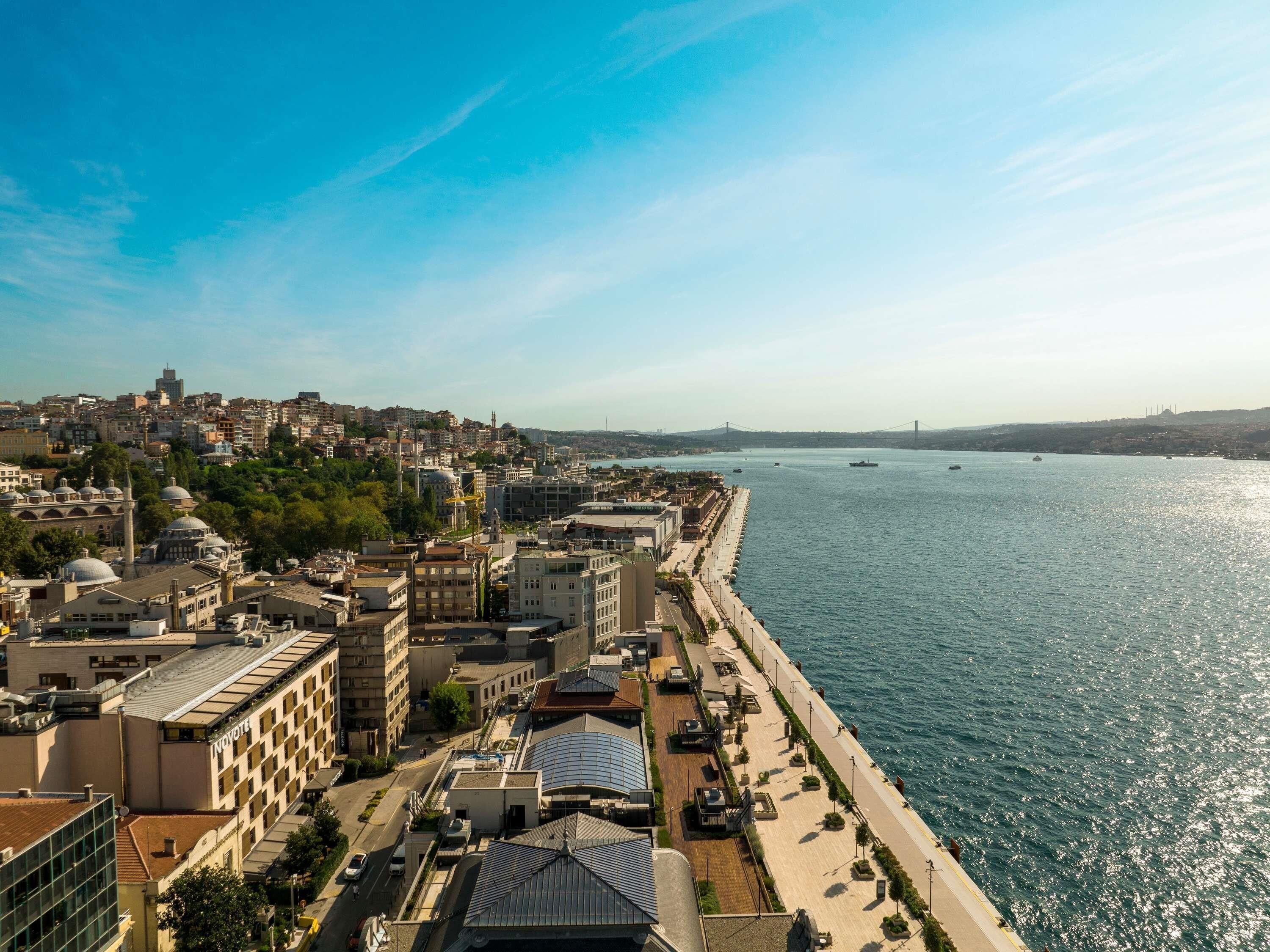 Un paisatge urbà costaner amb una destacada passeig marítim, edificis històrics i un pont a la distància.