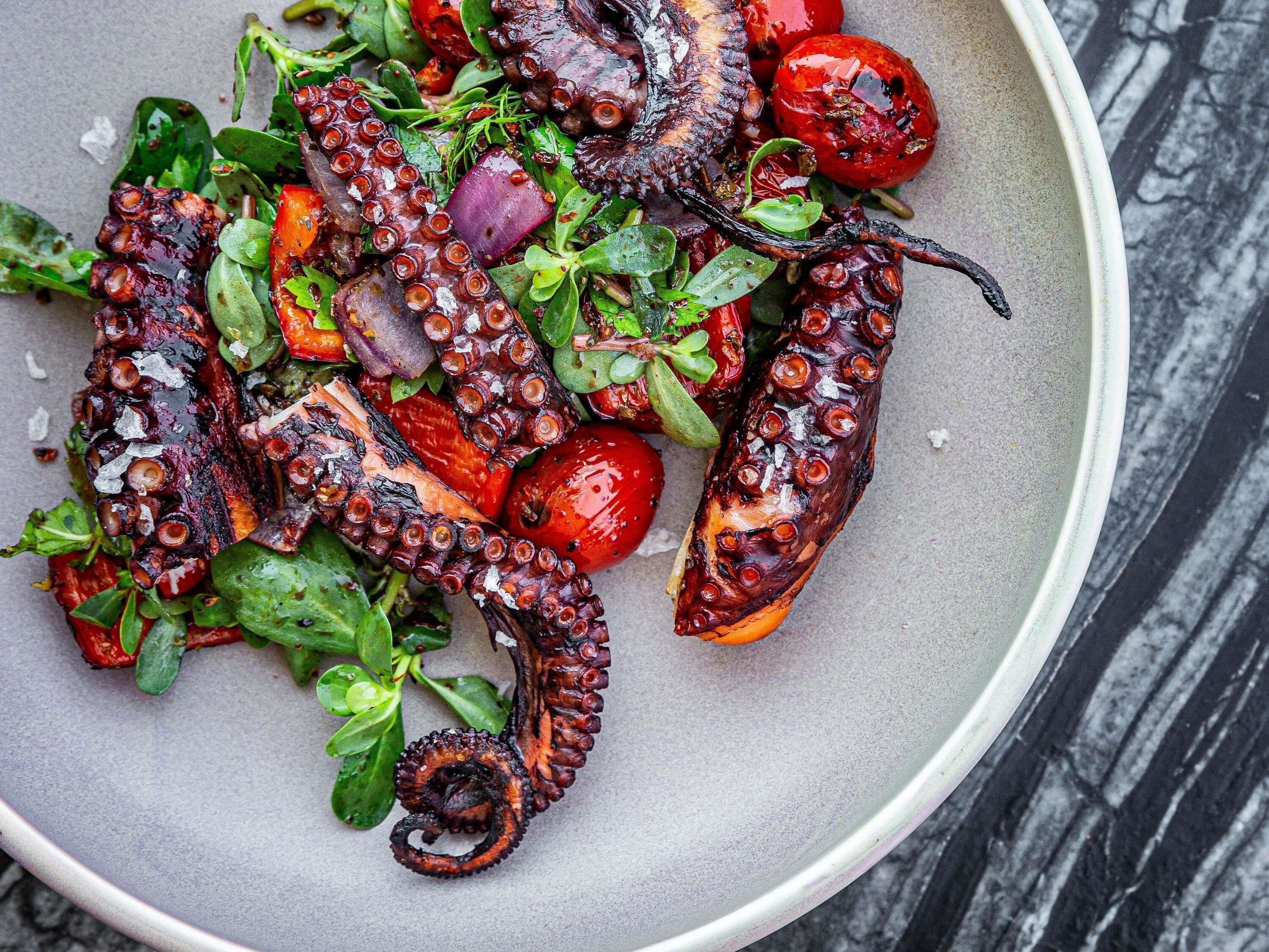En tallerken med grillet blæksprutte og grøntsager.