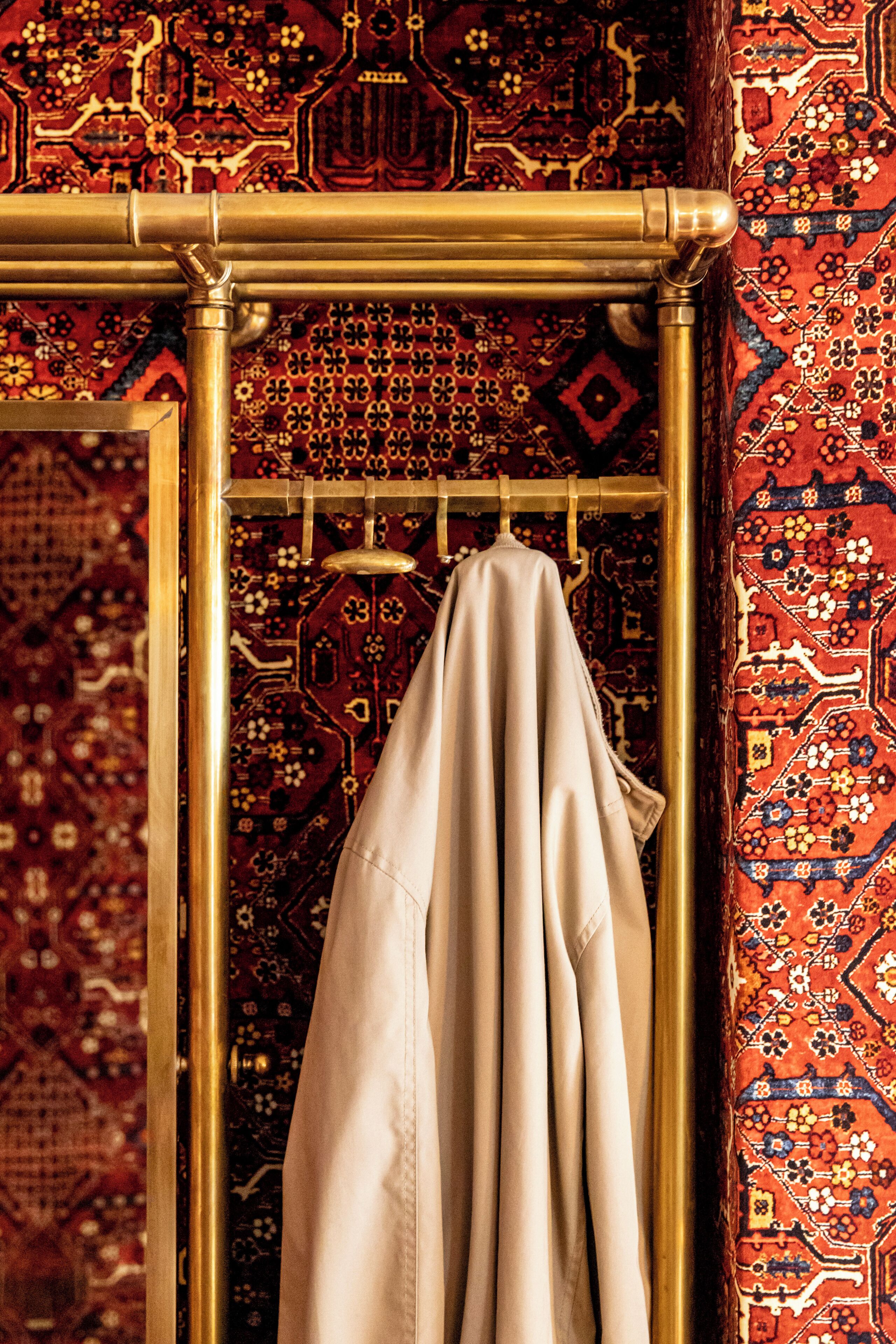 Una habitación con alfombra estampada, una toalla beige colgada en un toallero dorado y una puerta de madera.