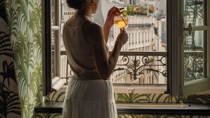A person standing by a window with a view of buildings, holding a drink. - Hôtel Providence (Paris)