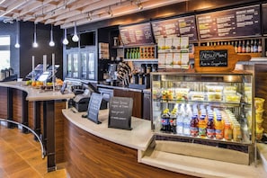 A modern coffee shop interior with a counter, menu boards, and a display case with beverages. - Courtyard by Marriott Columbus Grove City (Grove City)