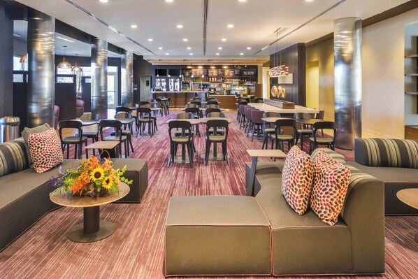 Un moderno vestíbulo de hotel con zona de bar, arreglos de asientos y un centro de flores.