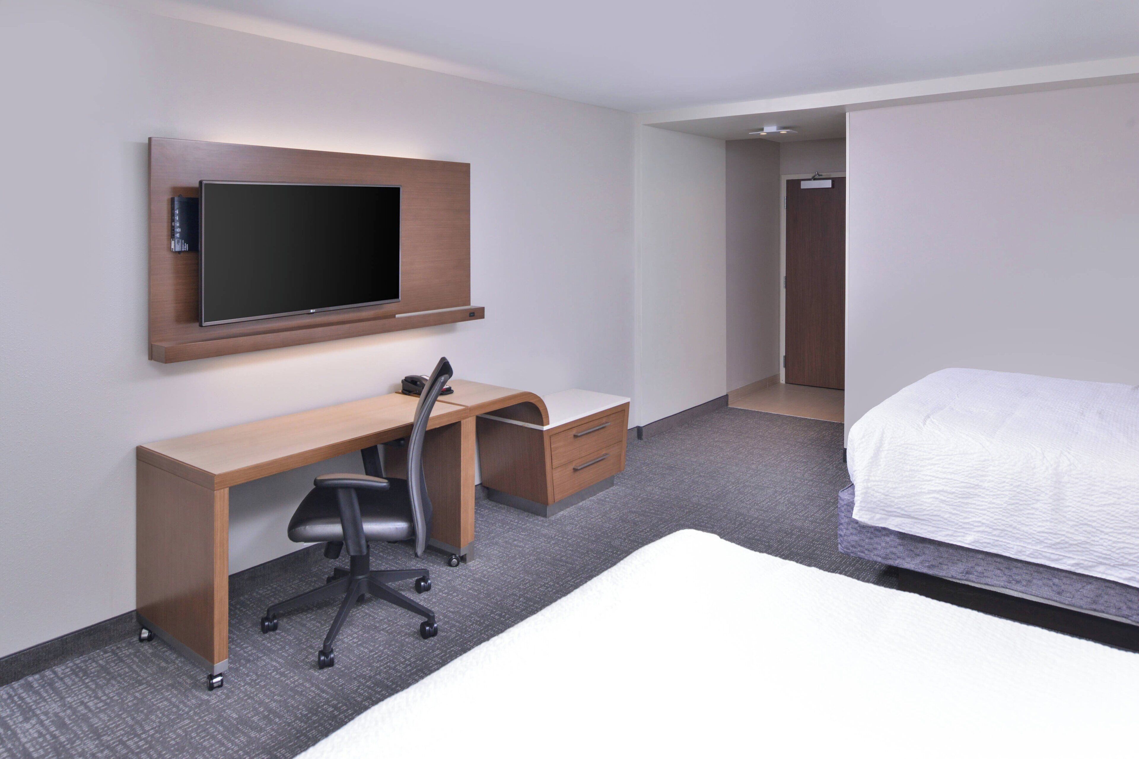 Habitación de hotel con cama, escritorio con silla, televisor montado en la pared y armario.