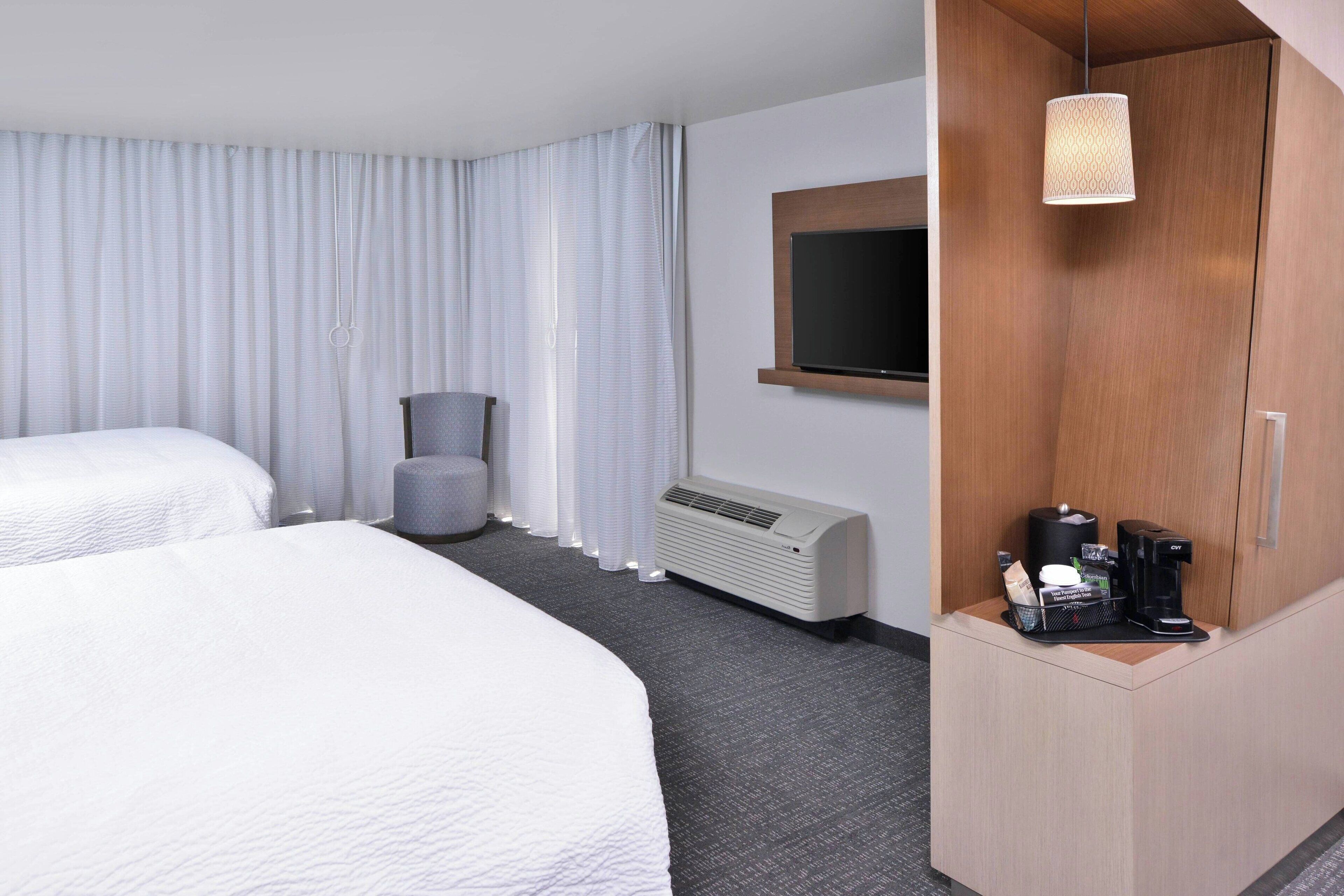 A hotel room with two beds, a desk with a coffee maker, a TV, and a window with curtains.