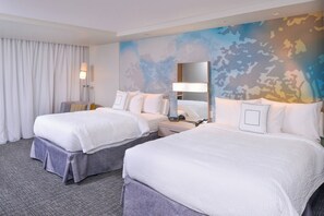 Habitación de hotel con dos camas, un espejo grande, una mesita de noche y una lámpara.