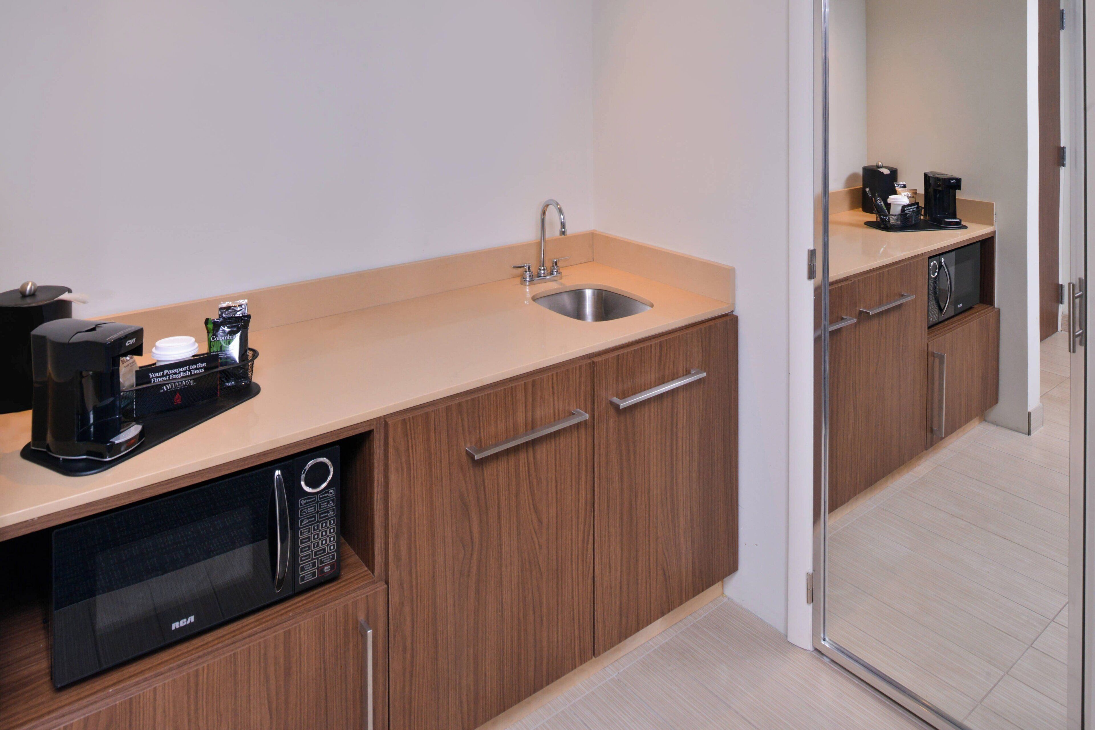 A compact kitchenette with a sink, microwave, coffee maker, and storage cabinets.