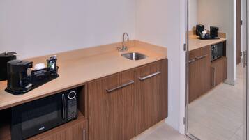 A compact kitchenette with a sink, microwave, coffee maker, and storage cabinets.
