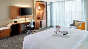 Une chambre d’hôtel avec un grand lit, un bureau avec une chaise, une télévision et une fenêtre avec des rideaux.