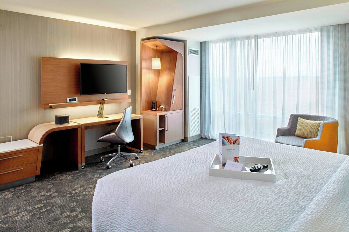 Une chambre d’hôtel avec un grand lit, un bureau avec une chaise, une télévision et une fenêtre avec des rideaux.