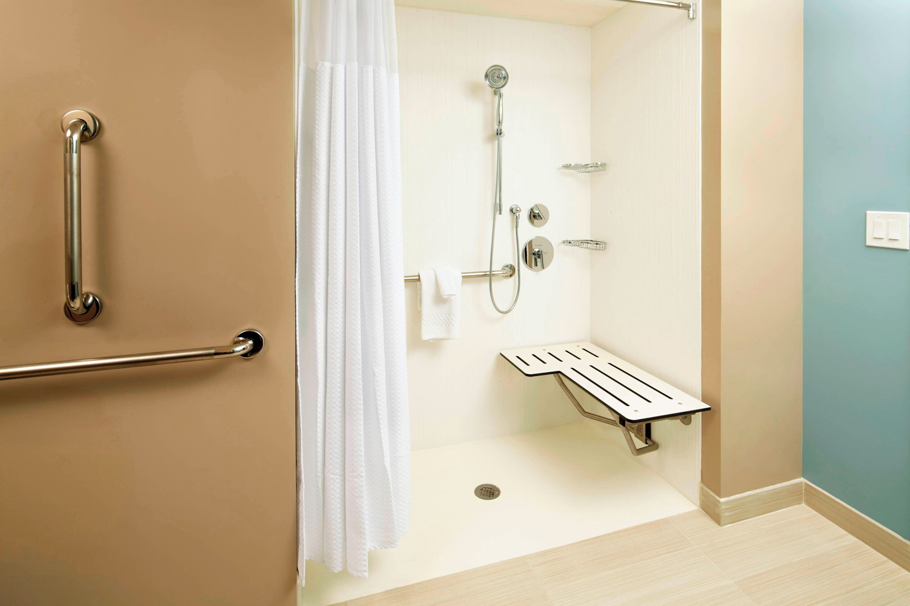 A bathroom with a shower, grab bars, a towel rack, and a toilet paper holder.