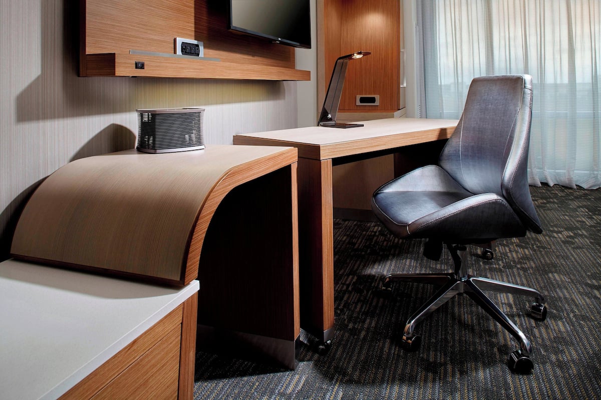 Une chambre d’hôtel avec un bureau en bois, un fauteuil de bureau en cuir, un téléviseur à écran plat fixé au mur et un petit haut-parleur.