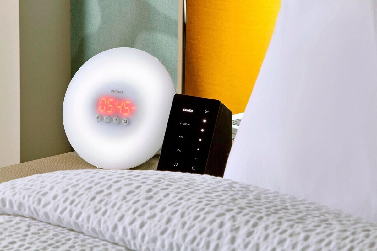 Eine Philips-Smart-Uhr und eine Circadian-Lampe auf einem Nachttisch mit einem weißen Kissen mit Struktur.