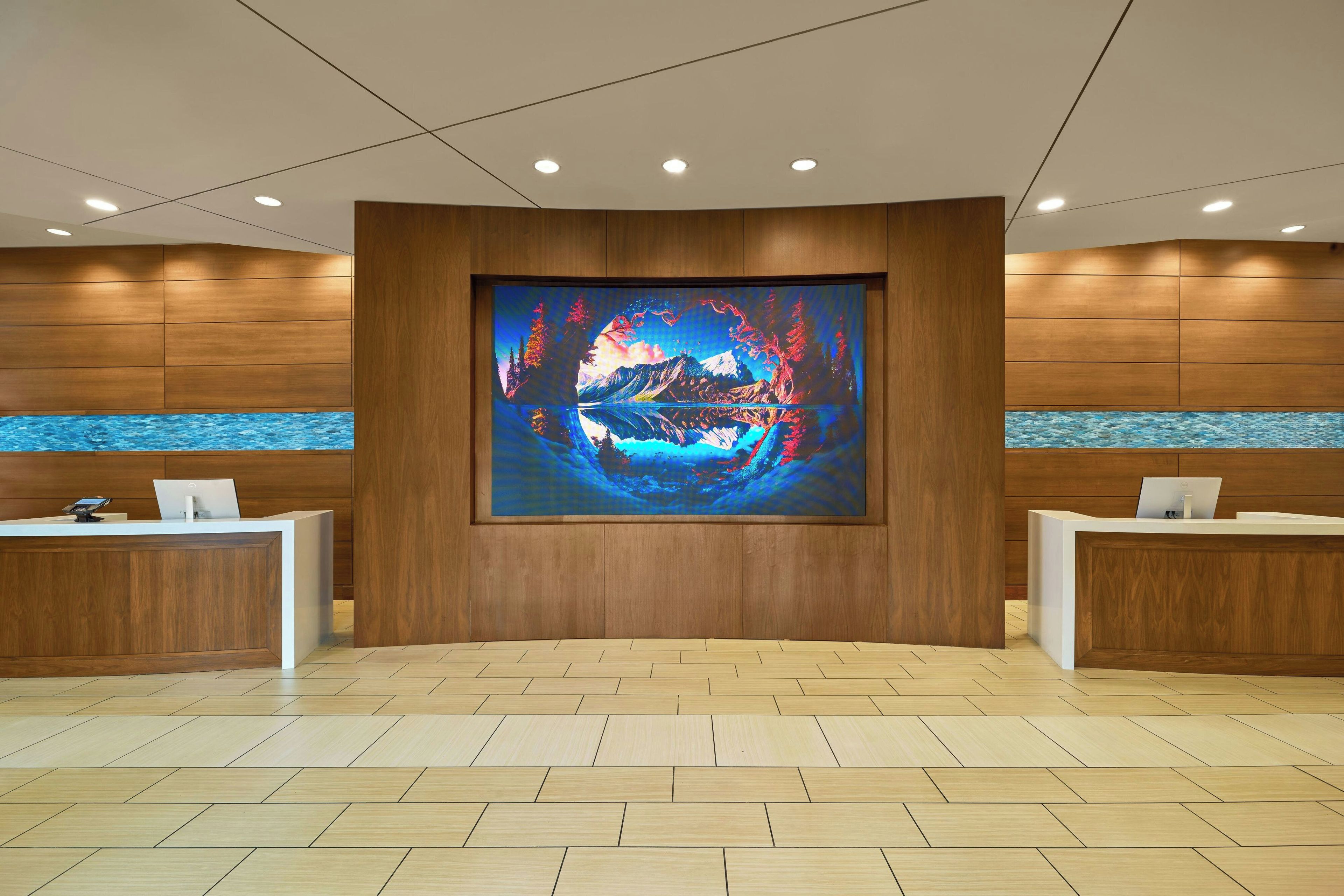 A reception area with a large digital art display, wooden paneling, and two reception desks.