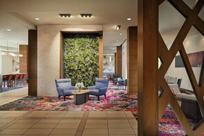 Un hall d’entrée agrémenté d’un jardin vertical, un espace détente avec des fauteuils, une table basse et une moquette à motifs.