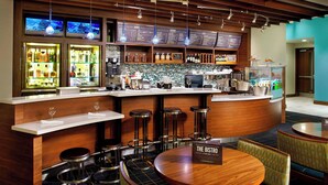 Un espace bar avec un comptoir en bois, des tabourets, une table ronde et un tableau affichant le menu.