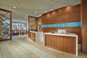 A reception area with a wooden reception desk, a blue mosaic wall, and a seating area with a sofa and chairs. - Courtyard Orlando Lake Nona (Orlando)