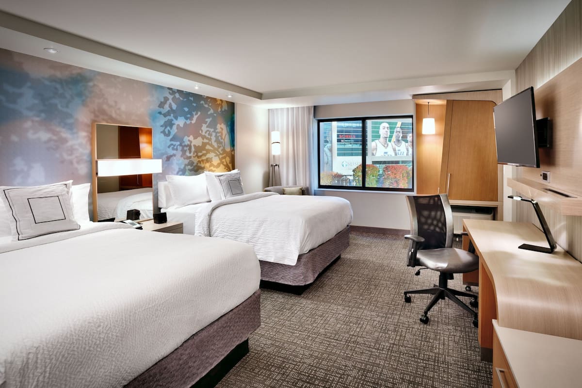 Ein Hotelzimmer mit zwei Betten, einem Schreibtisch, einem Sessel, einem Fernseher und einem großen Fenster mit Blick.