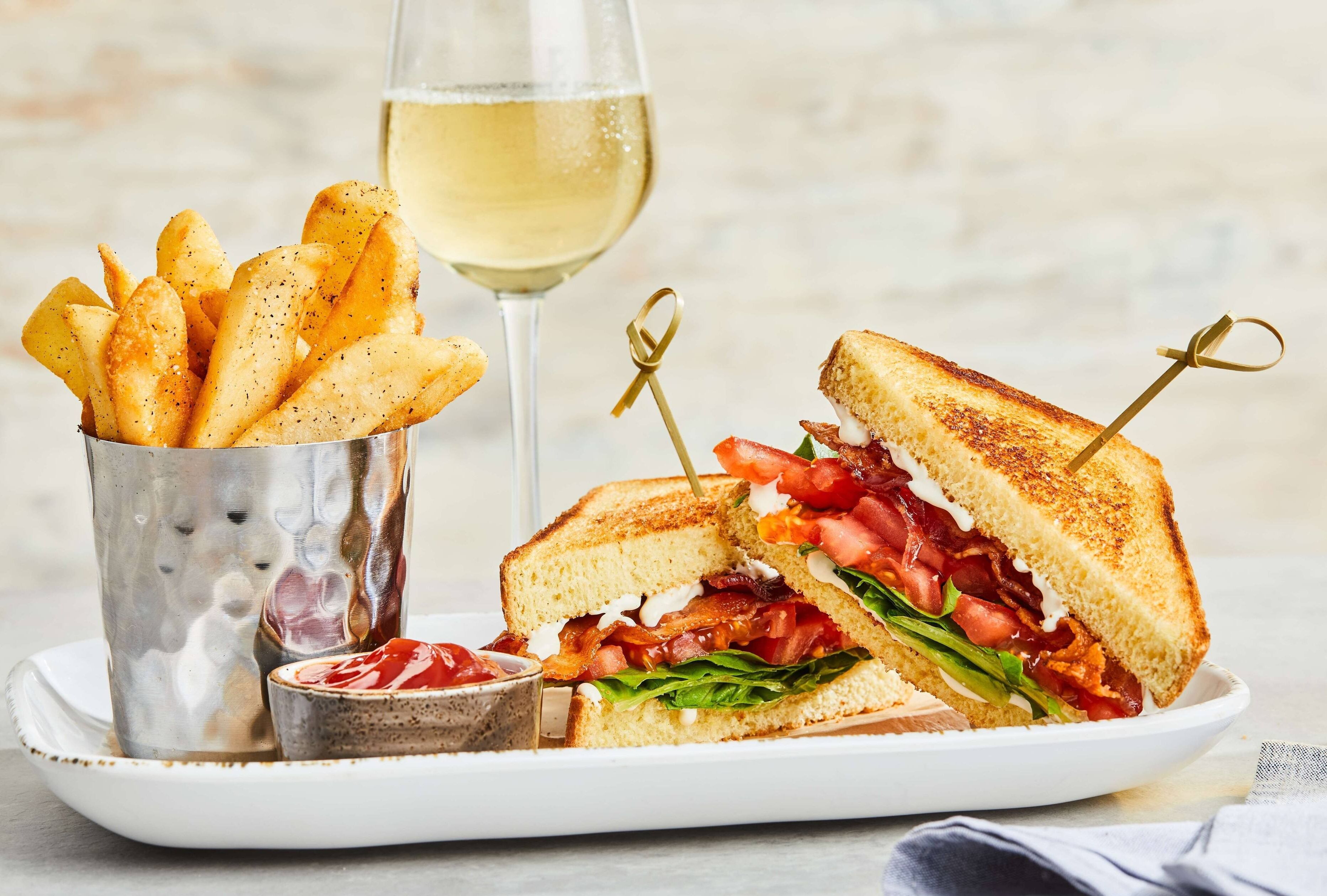 A sandwich with a side of fries and a glass of white wine on a plate.