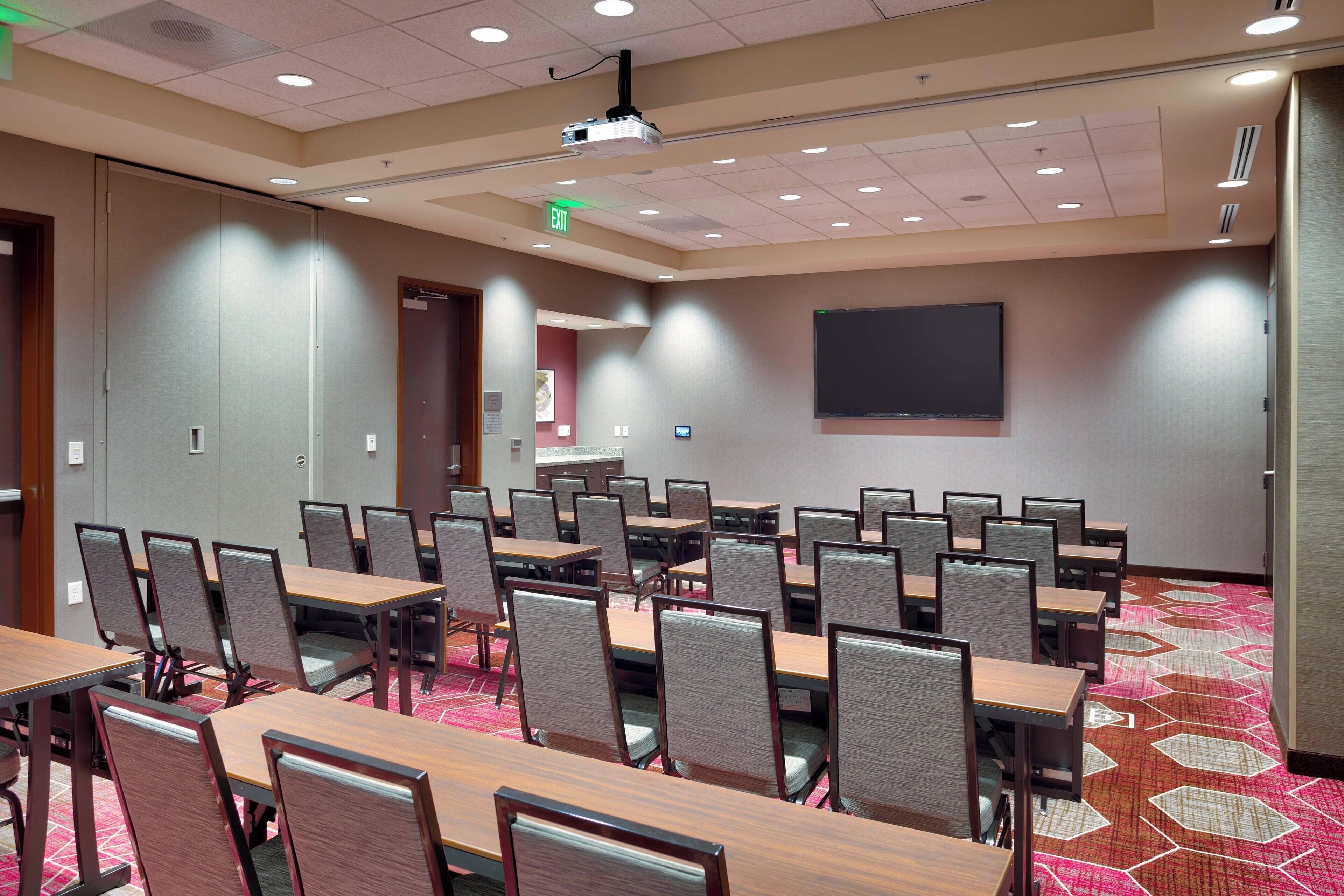A conference room with multiple tables and chairs, a projector, and a large screen on the wall.