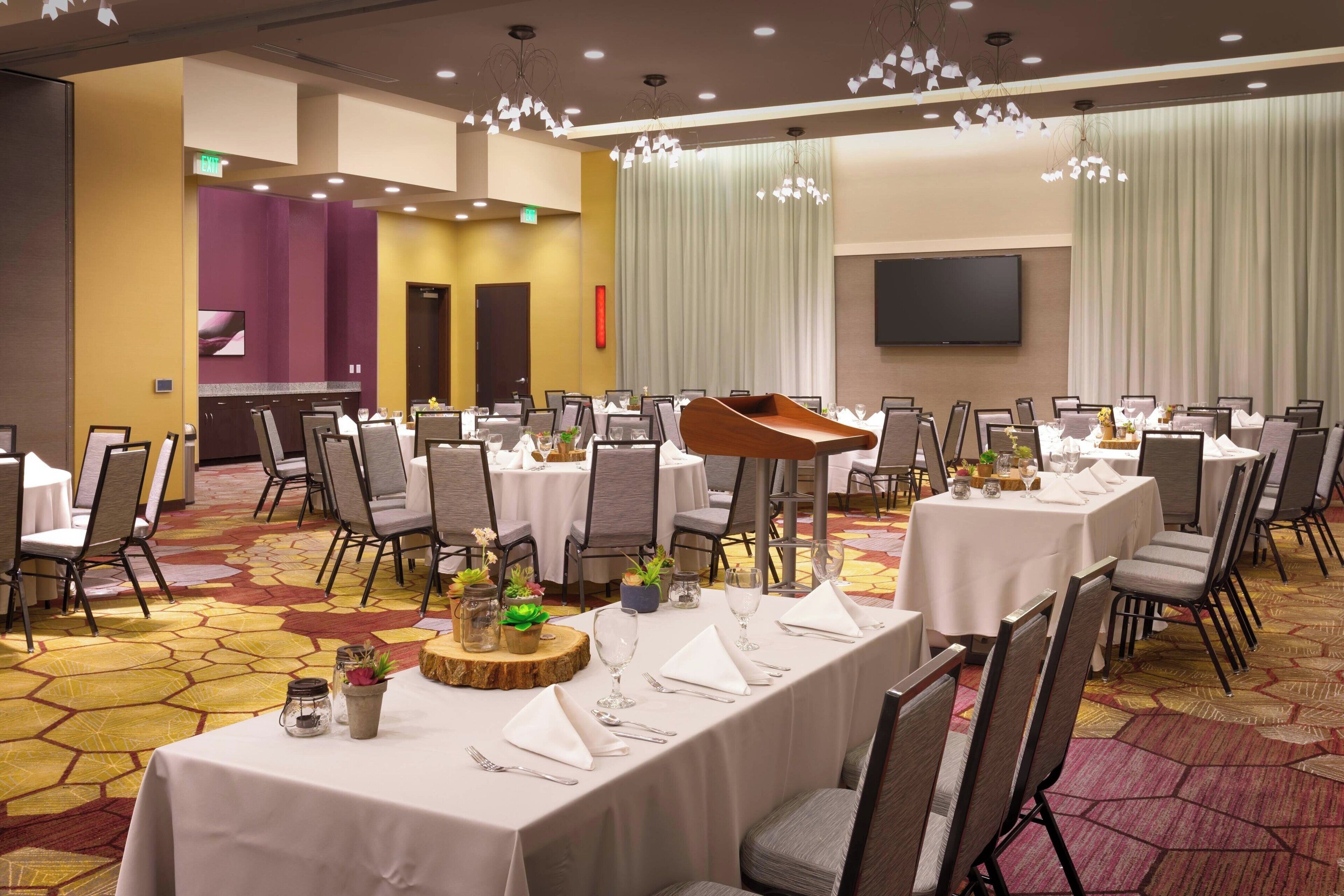 A banquet hall with multiple round tables set for dining, equipped with chairs and white tablecloths.