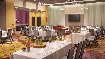A banquet hall with multiple round tables set for dining, equipped with chairs and white tablecloths.