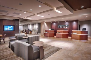 A modern hotel lobby with a reception desk, seating area, and a large screen displaying information.