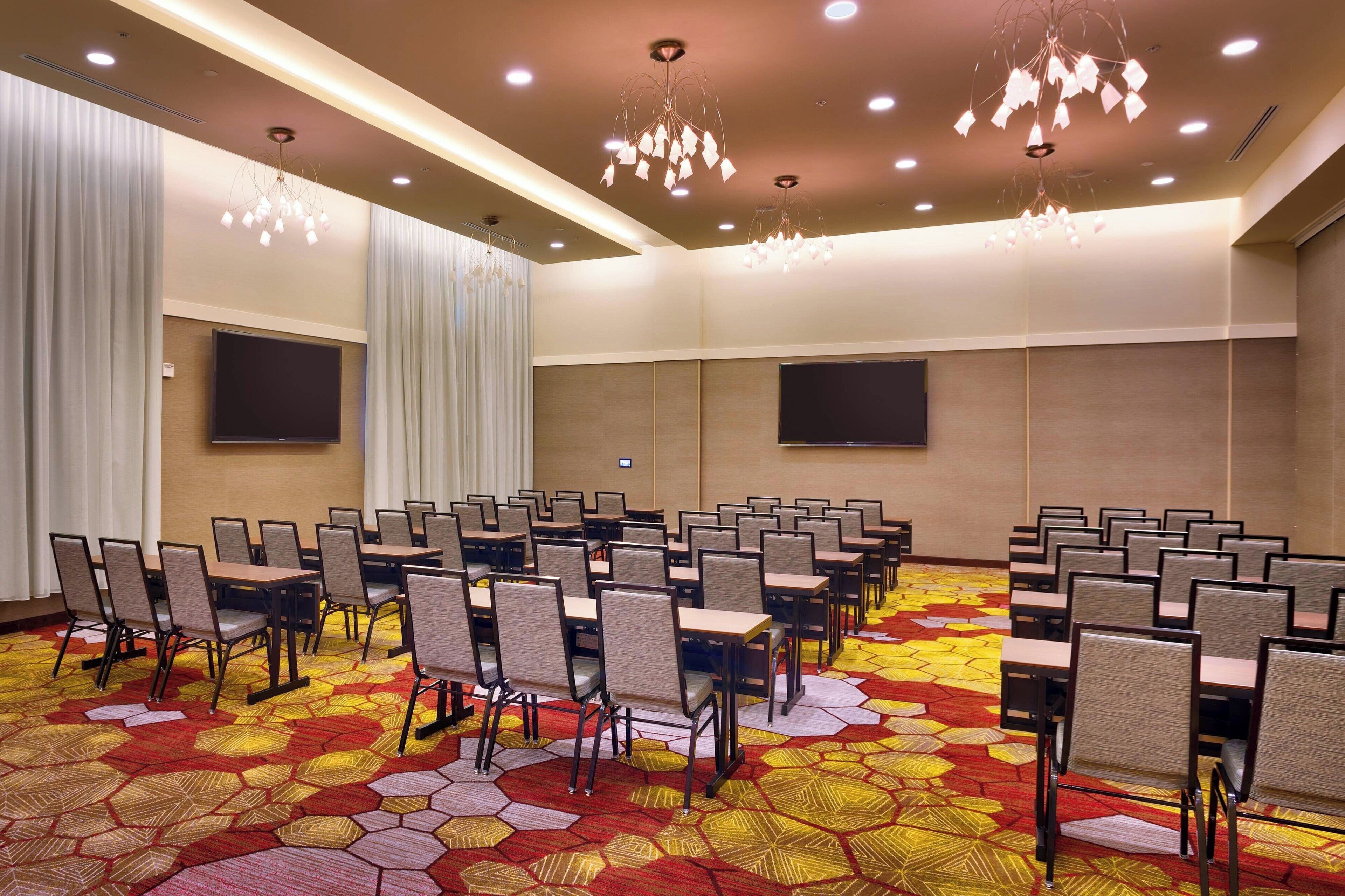 A conference room with rows of chairs, a large flat-screen TV, and a patterned carpet.