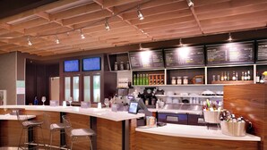 A modern bar area with a wooden counter, bar stools, and a menu board. - Courtyard Salt Lake City Downtown (Salt Lake City)