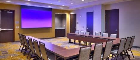 A conference room with a long table, chairs, a projector screen, and a carpeted floor.